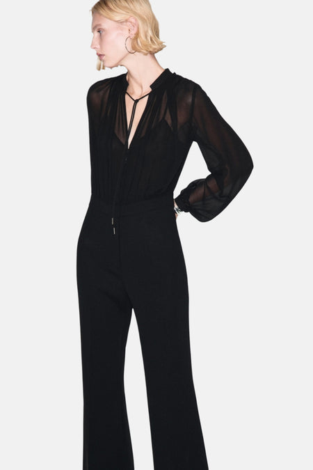 Combinaison noire par MANGO, avec un haut transparent à manches longues et un pantalon évasé.