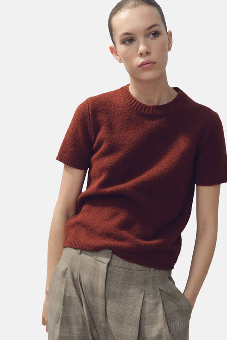 Pull à col rond brun de MANGO, en maille texturée, porté avec un pantalon à carreaux taille haute.
