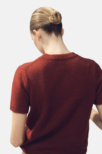 Pull à col rond brun de MANGO, tricot texturé, porté avec les cheveux relevés en chignon, vue de dos.