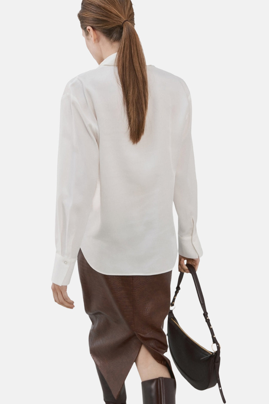 Chemise à manches longues blanche de MANGO, avec des manches longues, portée avec une jupe marron et un sac à main.