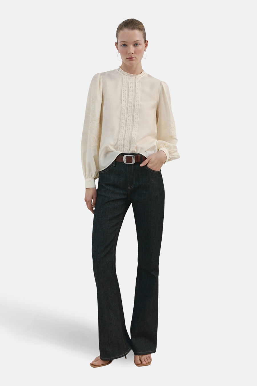Ecru blouse (lange mouwen) van MANGO, versierd met verticale kant en gedragen met een high-waisted jeans en een bruine riem.