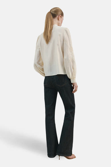 Ecru blouse met lange mouwen van MANGO, versierd met bloemenborduursels en gedragen met een uitlopende jeans.