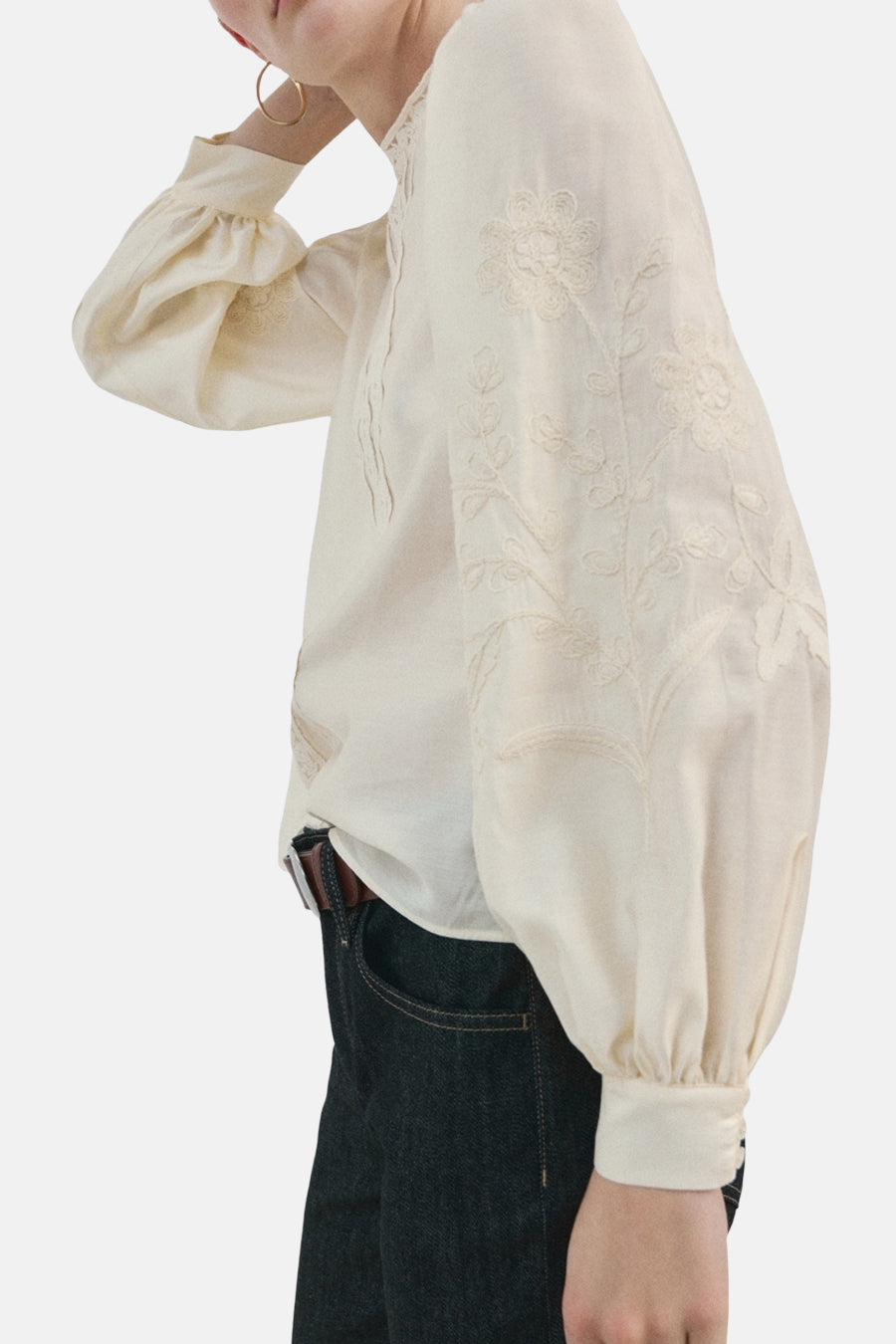 Ecru blouse met lange mouwen van MANGO, met bloemenborduursels en gedragen met een donkere jeans en een bruine riem.