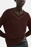 Pull à col en V brun de MANGO, orné d'une bordure blanche contrastante au col, porté avec une jupe texturée.
