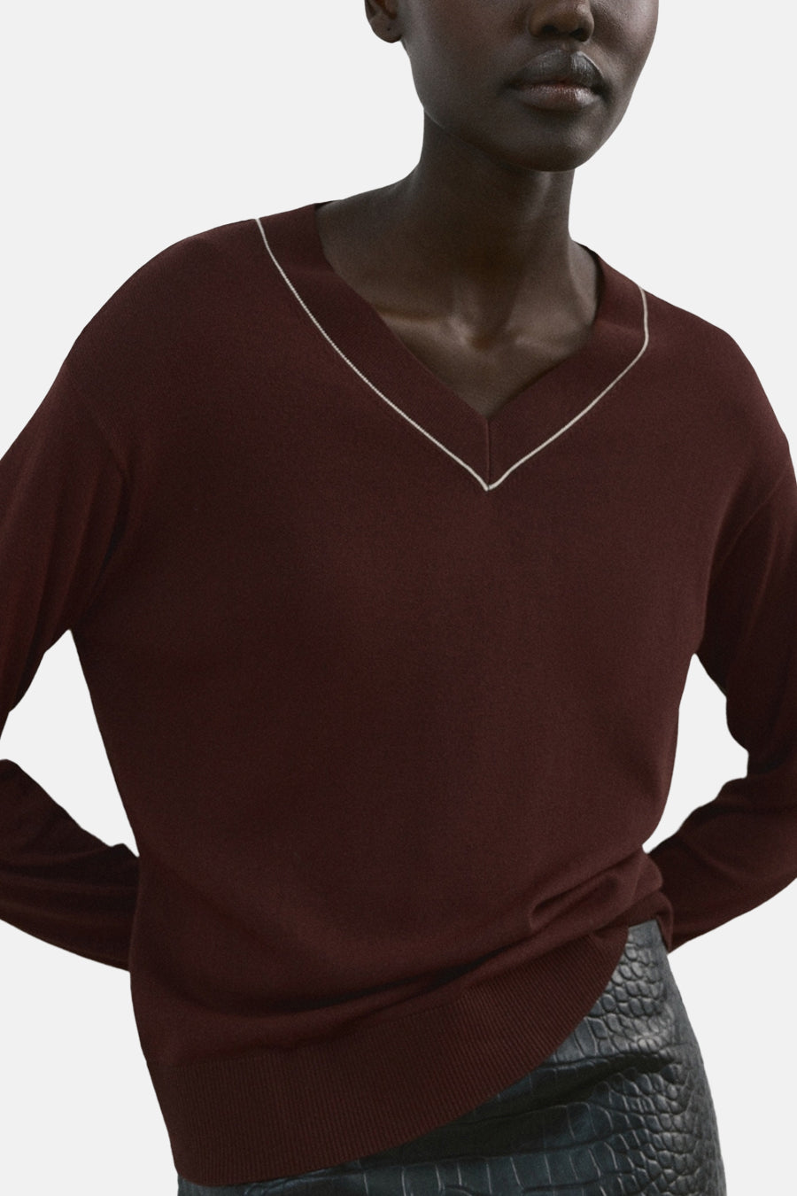 Pull à col en V brun de MANGO, orné d'une bordure blanche contrastante au col, porté avec une jupe texturée.

