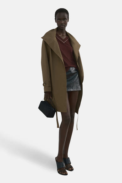 Pull à col en V brun de MANGO, porté avec une jupe en simili cuir et un manteau long.