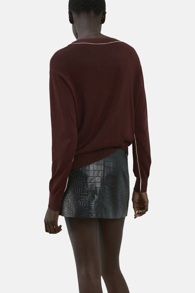 Pull à col en V brun de MANGO avec liseré blanc, porté avec une minijupe en similicuir crocodile.