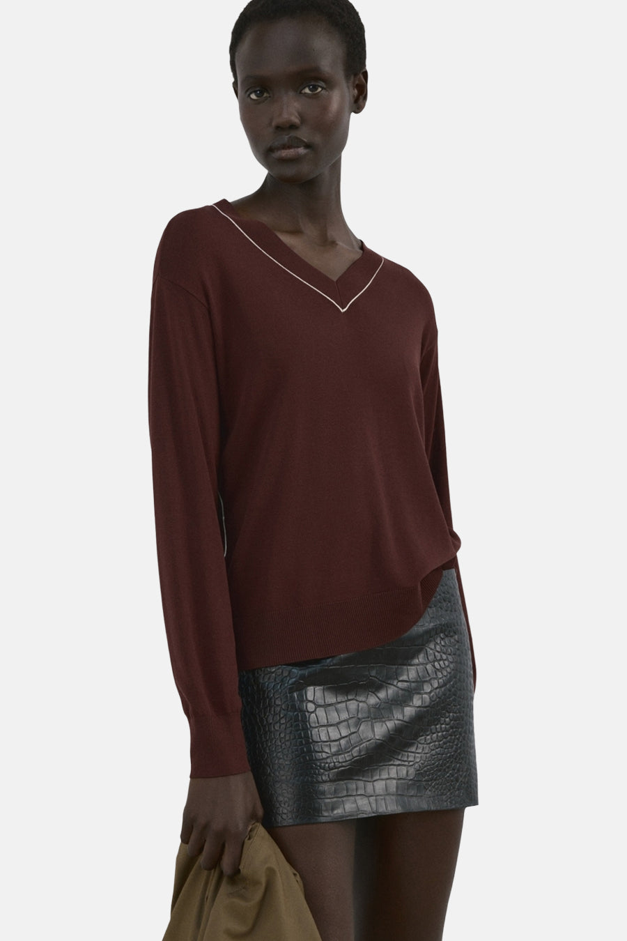 Pull à col en V brun de MANGO, bordure blanche au col, porté avec une jupe en cuir effet crocodile.