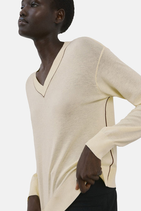 Pull à col en V jaune de MANGO, avec bordure contrastante marron au col et aux manches.
