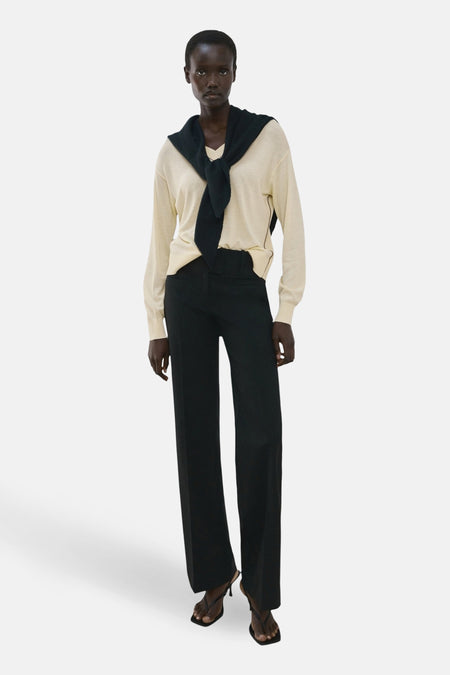 Pull à col en V jaune par MANGO porté avec un autre pull noir noué autour du cou, et un pantalon noir.
