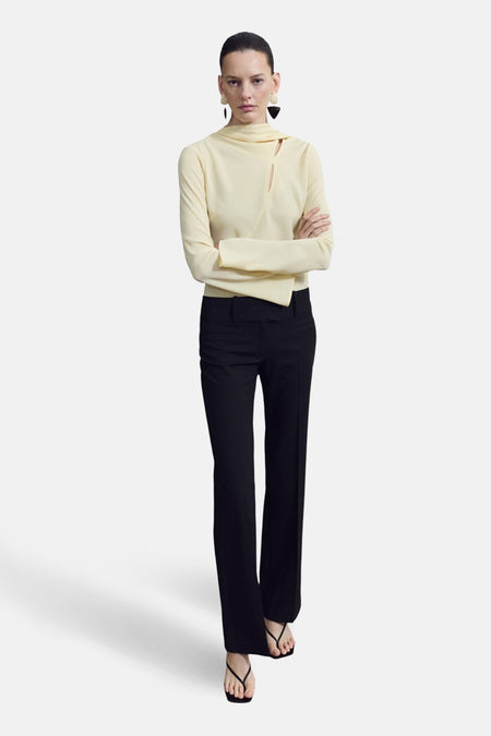 Blouse à manches longues jaune de MANGO, avec col montant et découpe sur le devant, portée avec un pantalon noir.