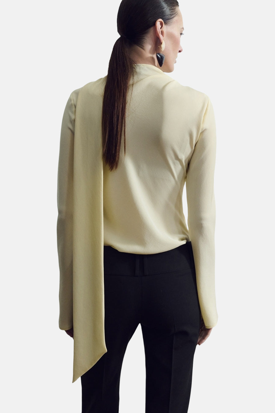 Blouse jaune à manches longues de MANGO, vue de dos, avec un long pan tombant et portée avec un pantalon noir.
