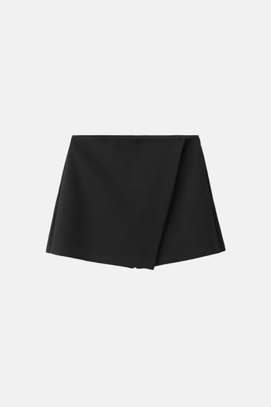 Jupe courte noire de MANGO, avec une coupe portefeuille asymétrique moderne.