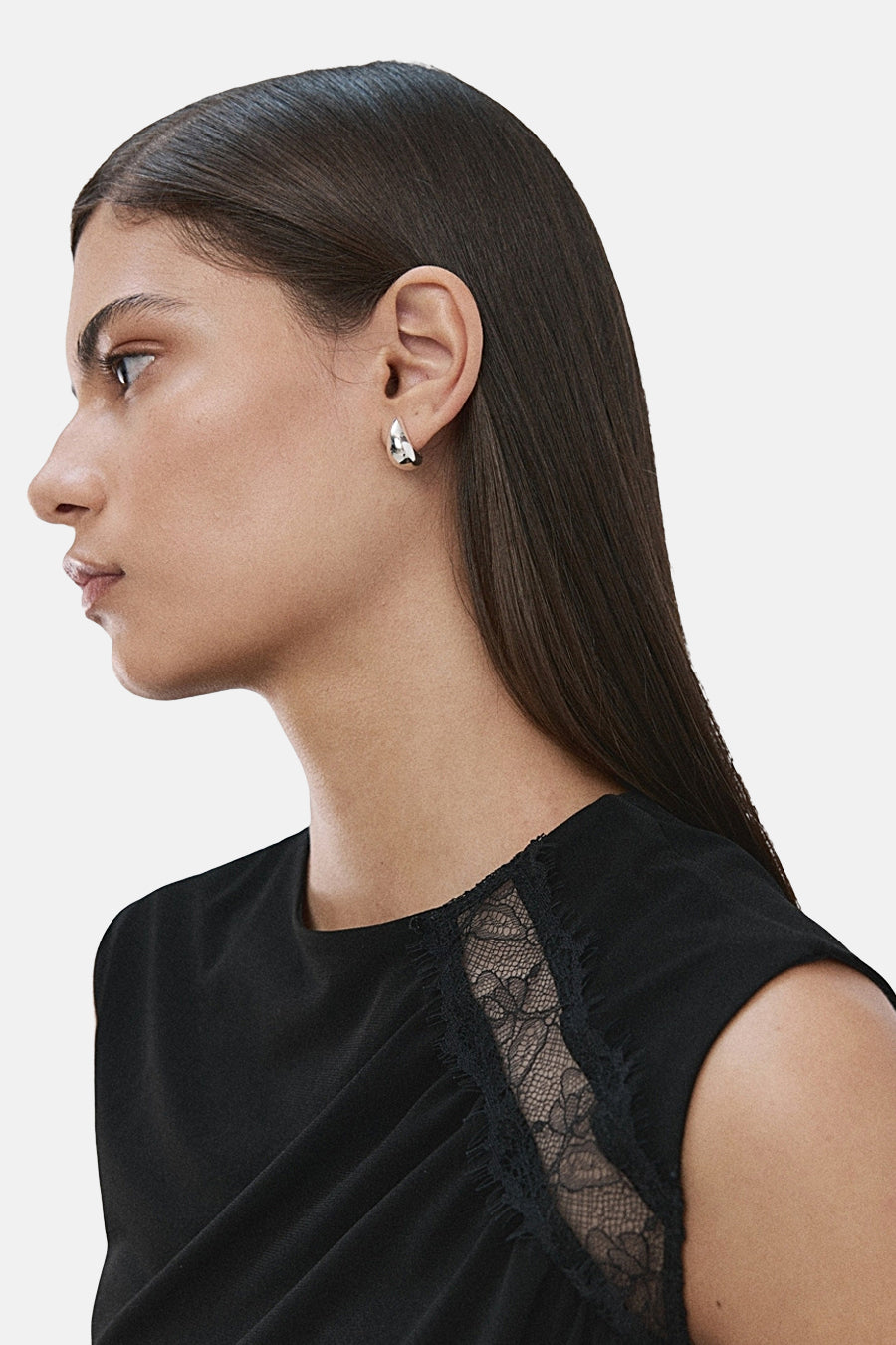 Blouse noire sans manches de MANGO, ornée d'une dentelle sur le côté, portée par un mannequin de profil.
