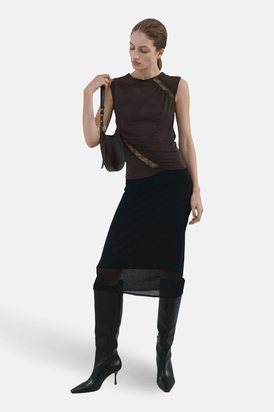 Chemisier sans manches brun MANGO avec détails en dentelle, porté avec une jupe noire transparente et des bottes en cuir.