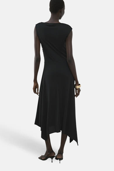Robe noire fluide de MANGO, avec une coupe asymétrique et un bracelet doré.