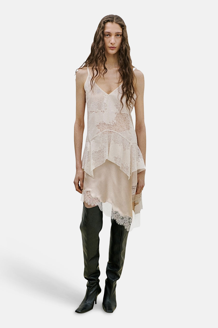 Top écru à fines bretelles de MANGO, avec motifs de dentelle et ourlet asymétrique, porté avec des bottes noires.