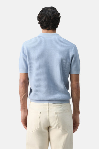 Polo bleu à manches courtes de MANGO, détail de la texture gaufrée, porté avec un pantalon beige clair, vue de dos.
