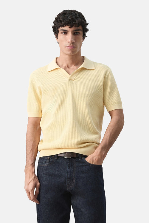 Polo à manches courtes jaune de MANGO, porté avec un jean foncé et une ceinture marron.
