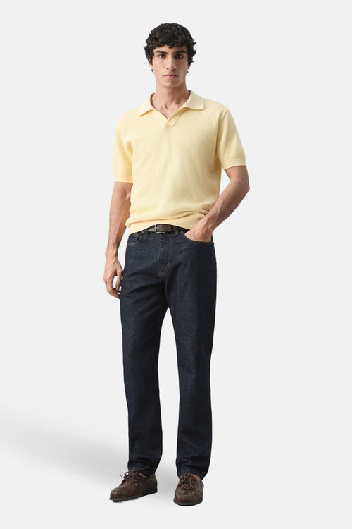 Polo à manches courtes jaune de MANGO, porté avec un jean bleu foncé et des chaussures bateau marron.