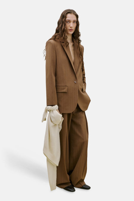 Bruine blazer van MANGO, open gedragen met een bijpassende broek en een sjaal om de pols geknoopt.