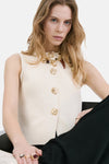 Beige gilet van MANGO, gebreid met openwerkdetails bij de armsgaten, gedragen met een wijde zwarte broek.