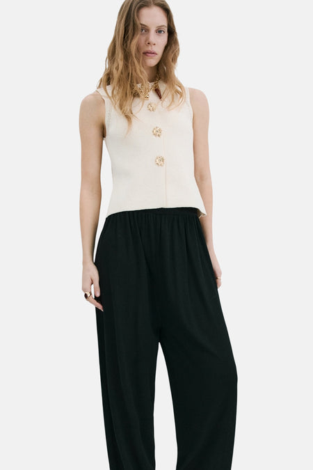 Gilet beige de MANGO orné de boutons décoratifs dorés, porté avec un pantalon noir ample et un collier doré.