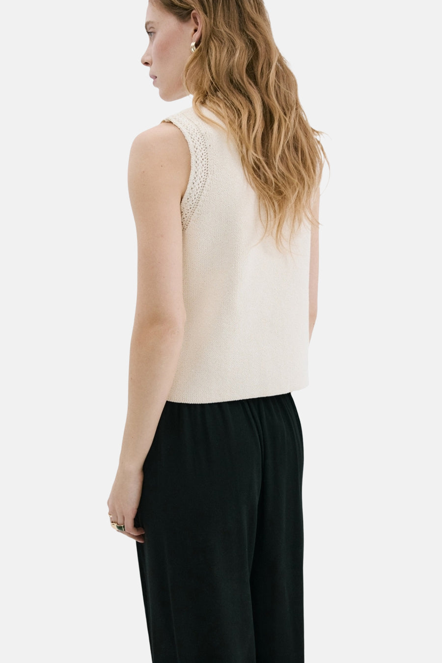 Gilet beige de MANGO, tricoté avec détails ajourés aux emmanchures, porté avec un pantalon noir ample.