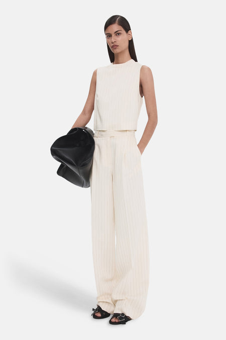 Pantalon blanc à rayures verticales de MANGO, coupe large, porté avec un haut sans manches et des sandales noires.