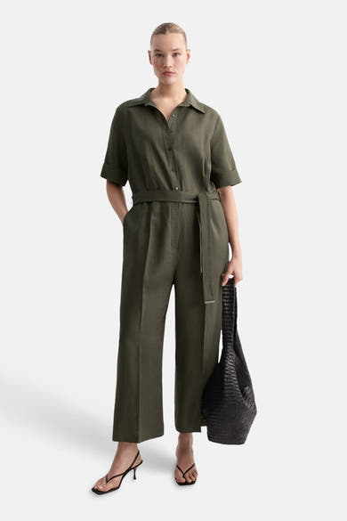Combinaison marron de MANGO, avec une ceinture assortie, portée avec des sandales à talons et un sac fourre-tout noir.
