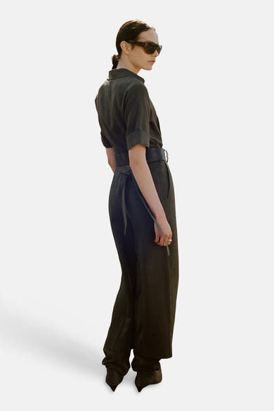 Combinaison brune de MANGO, avec ceinture nouée et manches courtes retroussées, portée avec des lunettes de soleil.