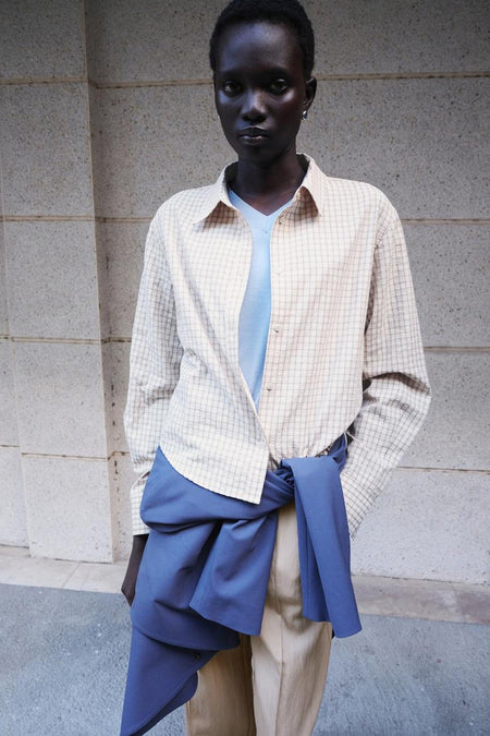 Chemise beige à carreaux de MANGO, portée ouverte sur un haut bleu clair avec un vêtement bleu noué à la taille.