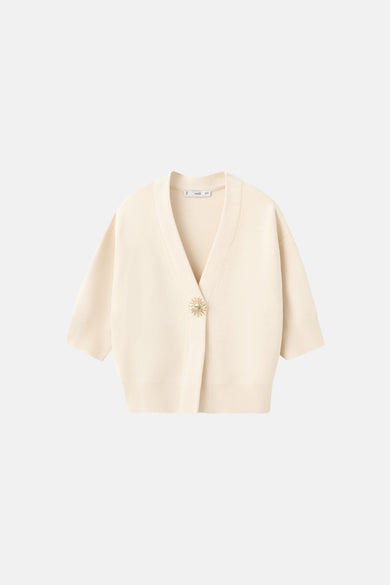 Gilet beige de MANGO, avec un bouton décoratif doré en forme de fleur.