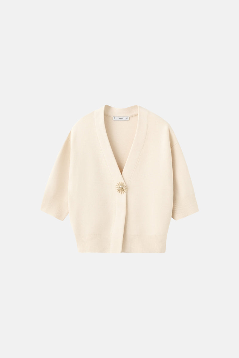 Gilet beige de MANGO, avec un bouton décoratif doré en forme de fleur.