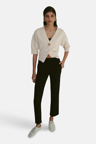 Gilet beige de MANGO, boutonné avec un ornement doré, porté avec un pantalon noir et des chaussures en toile.
