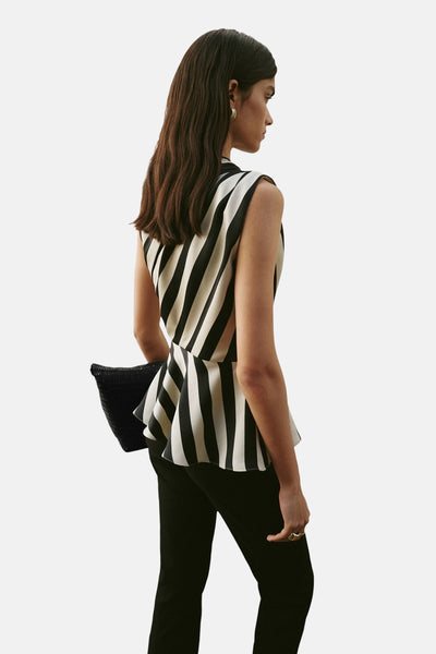 Blouse sans manches multicolore de MANGO, à rayures verticales noires et crème, portée avec un pantalon noir et une pochette tressée.