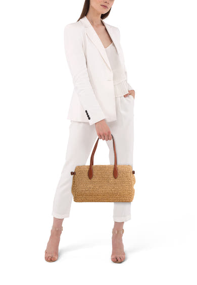 Beige schoudertas van MANGO, in de hand gedragen, met bruine leren details, gedragen met een wit broekpak.