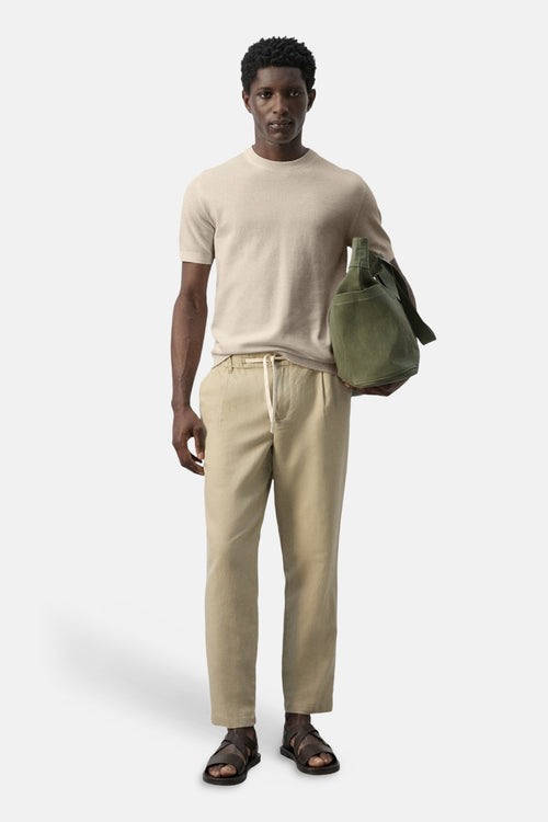 T-shirt beige à manches courtes de MANGO, porté avec un pantalon beige à cordon et des sandales croisées.