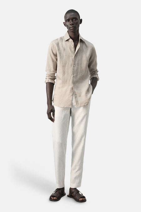 Chemise beige en lin de MANGO, portée avec un pantalon clair et des sandales en cuir.