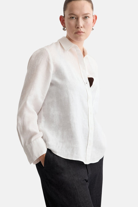 Chemisier en lin blanc de MANGO, avec manches longues et boutons, porté avec un pantalon foncé.