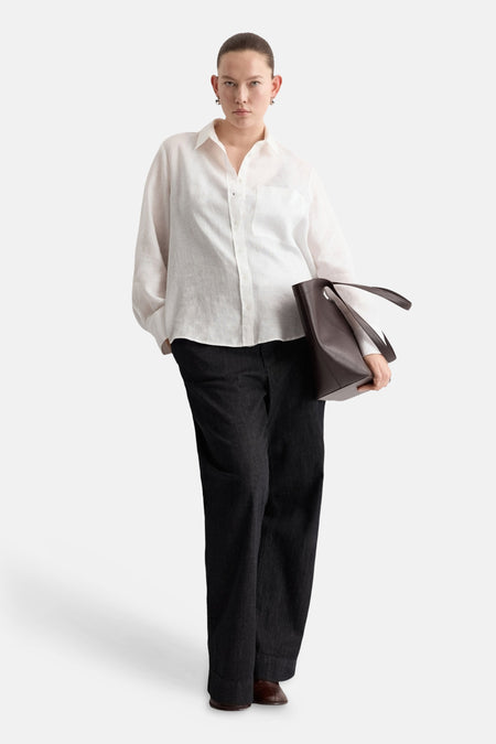 Chemisier blanc à manches longues de MANGO, porté avec un pantalon noir ample et un sac en cuir marron.
