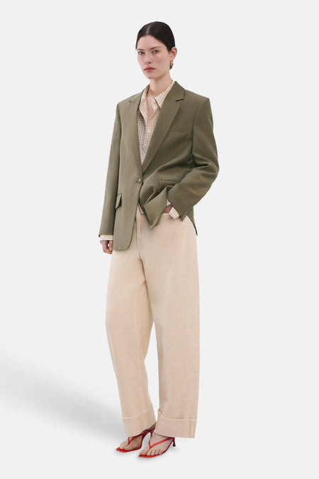 Kaki blazer van MANGO gedragen over een geruit overhemd, met een beige broek en rode sandalen.