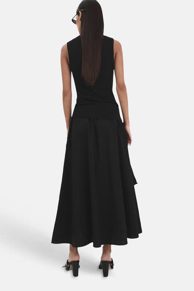 Jupe longue noire de MANGO, coupe fluide et évasée, portée de dos avec un top noir sans manches et des mules.