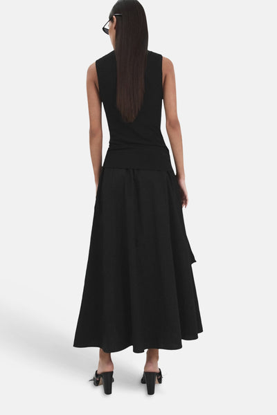 Jupe longue noire de MANGO, coupe fluide et évasée, portée de dos avec un top noir sans manches et des mules.