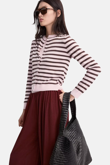 Gilet rayé rose clair et marron foncé de MANGO, boutonné, porté avec une jupe bordeaux et un sac tressé noir.