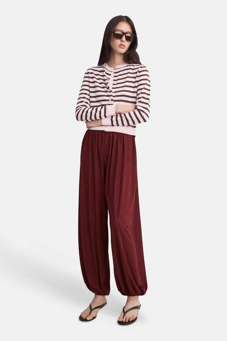 Gilet multicolore de MANGO, rayé rose et marron, porté avec un pantalon bordeaux et des tongs.