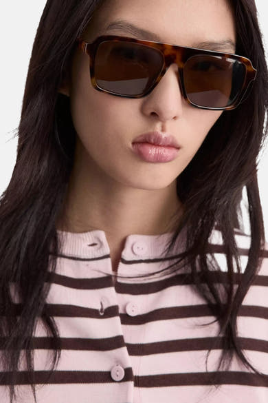 Roze en bruin gestreept vest van MANGO, met knopen, gedragen door een model met een zonnebril.