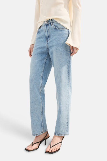 Jean droit en denim bleu clair de MANGO, porté avec un haut crème et des sandales noires à talons.

