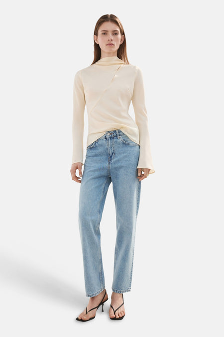 Jean droit en denim bleu clair de MANGO, porté avec un haut à col roulé couleur crème et des sandales à talons noirs.
