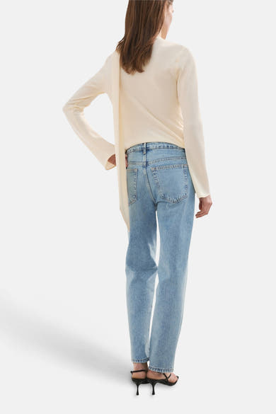 Jean droit en denim bleu clair de MANGO, porté avec un haut couleur crème et des sandales noires à talons.
